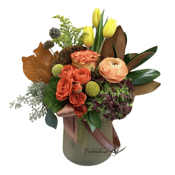 Welcome in the fall season with this fall theme flower arrangement.  It includes roses, spray roses, tulips, hydrangea, billy ball, salidago, greenery, and fall accents. All is arranged in a creamy yellow glass vase with decorative leather strap.